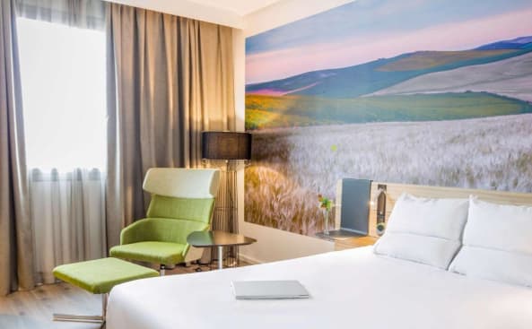 Habitación de hotel con cama y silla verde en Novotel Sevilla, en Sevilla