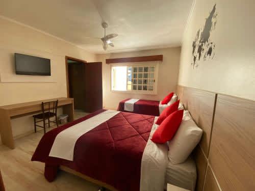 1 habitación con cama con almohadas rojas y escritorio en Casa do Rogerio Hostel - Unidade Shopping, en Caxias do Sul