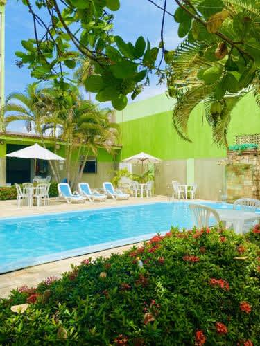 una piscina con sillas y sombrillas junto a un edificio en la Pousada o Caribe de Maragogi, en Maragogi