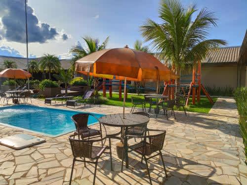 un patio con mesas y sillas y una sombrilla junto a la piscina del Hotel Pousada Parque das Águas, en Olímpia