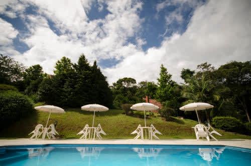 un grupo de sillas y sombrillas junto a una piscina en la Pousada Alpes, en Santo Antônio do Pinhal
