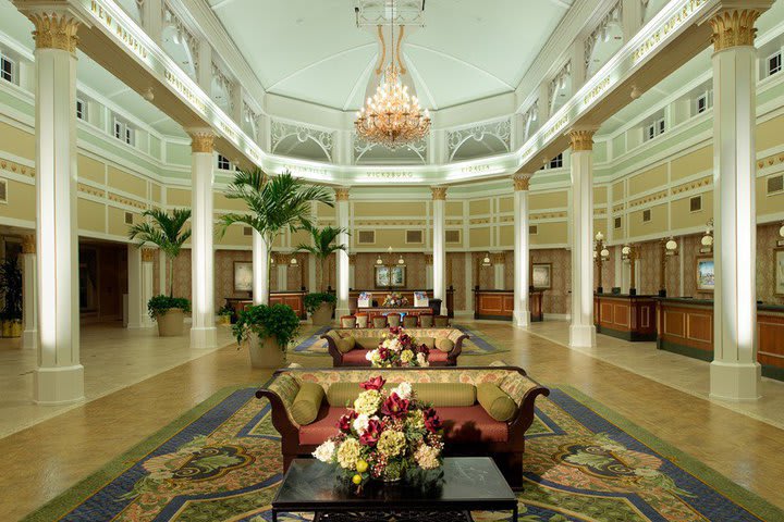 The lobby has white pillars, high ceilings, and chandeliers