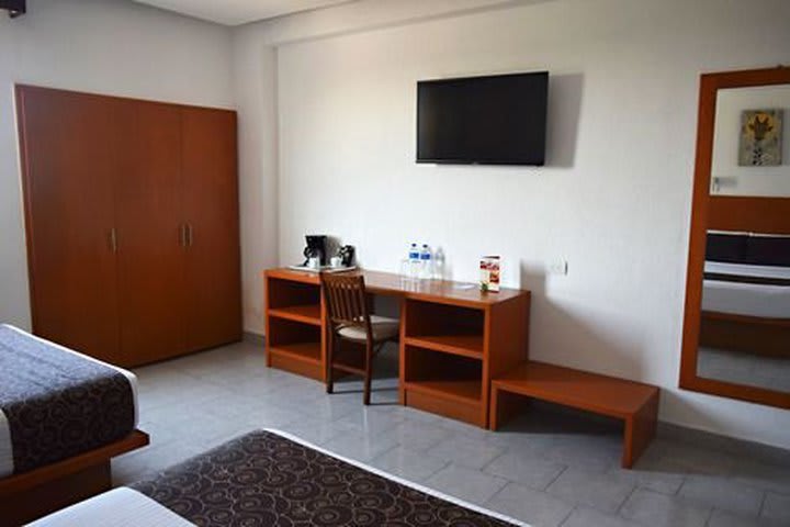 Vista de la habitación, cuenta con mesa de trabajo, televisión pantalla plana, cafetera y amenidades, armario y aire acondicionado